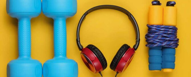 Minimalistic sport and fitness concept. Wired headphones and dumbbell, jump rope on yellow background.