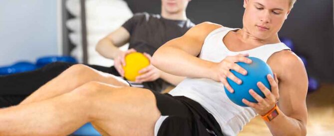 Focused young men doing sit ups on half ball and with medicine ball as weight at the fitness class. Core muscle and balance workout. Team and motivation at the gym.